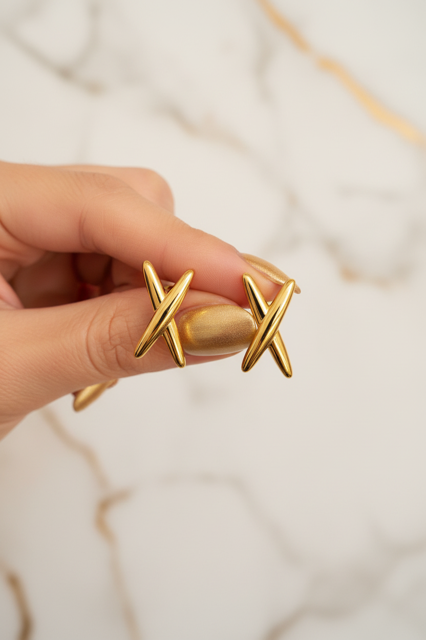 Main présentant les boucles d'oreilles croix dorées
